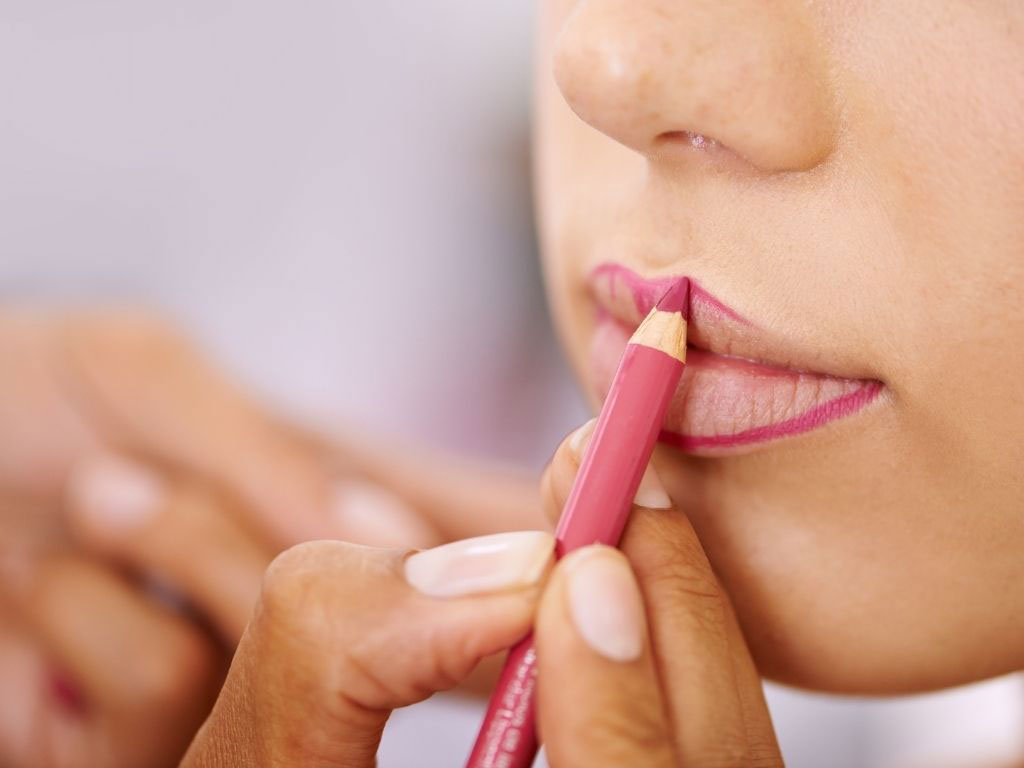 woman outlining her lips before applying lipstick